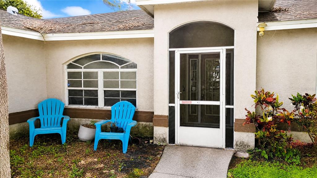 A house exterior features a screened front door, an arched window, and two blue chairs — 12021 68TH STREET, LARGO, FL