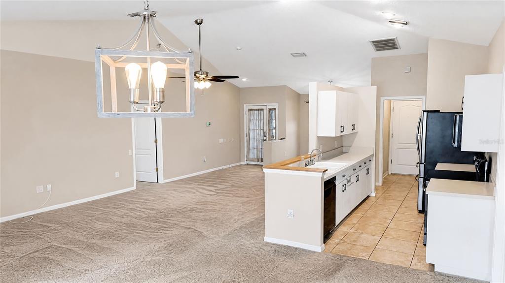 A kitchen with white cabinets and tile flooring opens into a carpeted living area — 12021 68TH STREET, LARGO, FL