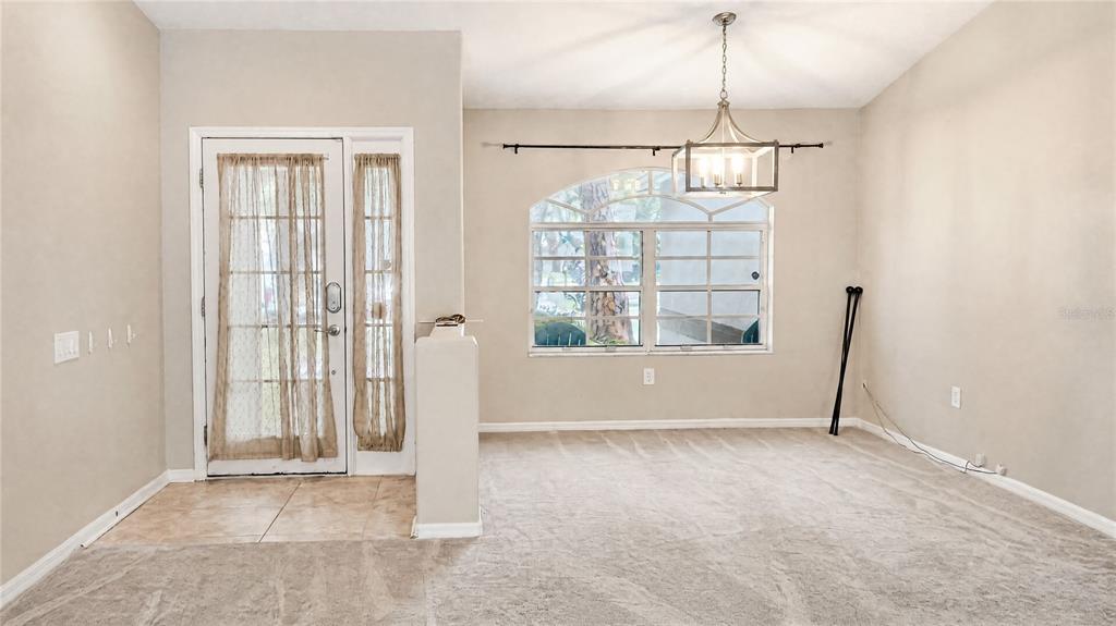 A dining room features beige carpeting, a chandelier, and a glass-paneled front door — 12021 68TH STREET, LARGO, FL