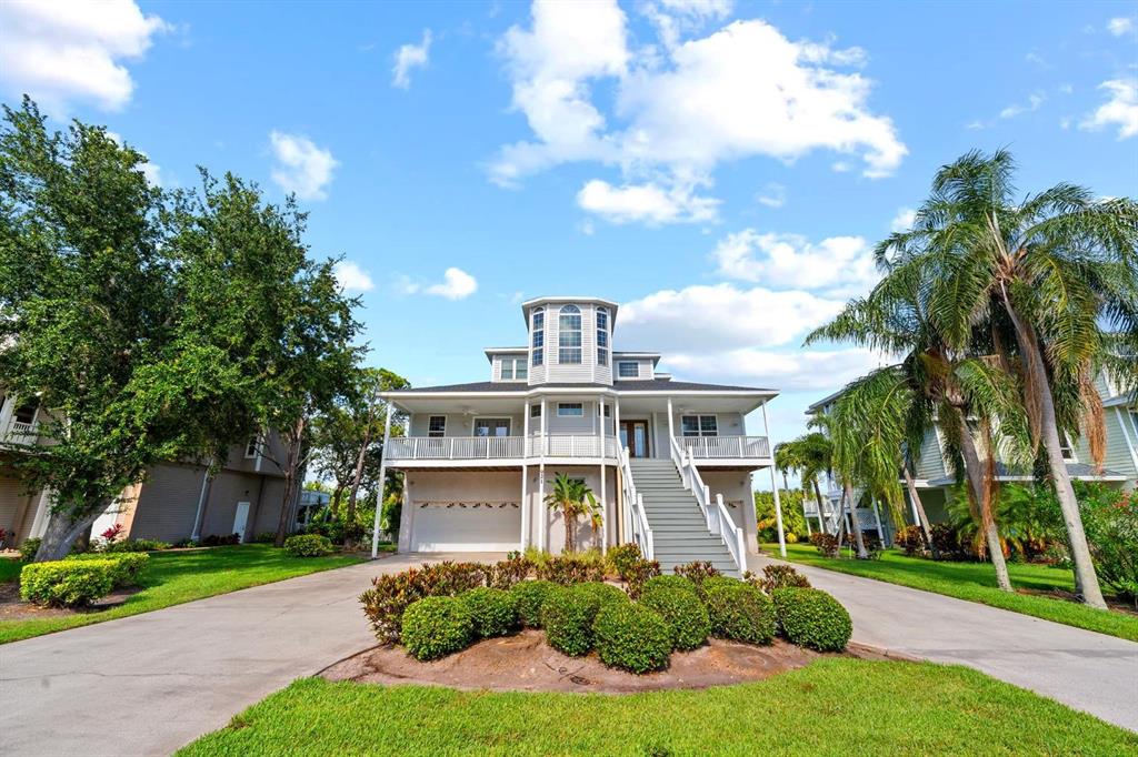 A three-story elevated house with a white exterior, a front staircase, and a concrete driveway — 921 POINT SEASIDE DRIVE, CRYSTAL BEACH, FL