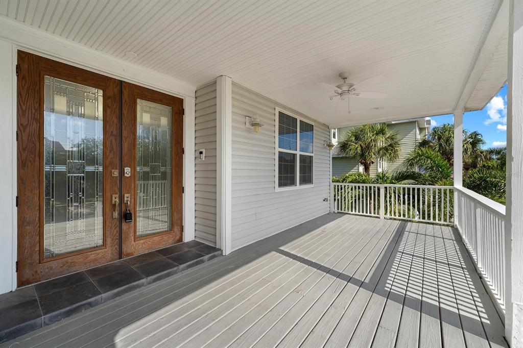 A covered wooden porch features double glass-paneled wood doors and a white railing — 921 POINT SEASIDE DRIVE, CRYSTAL BEACH, FL