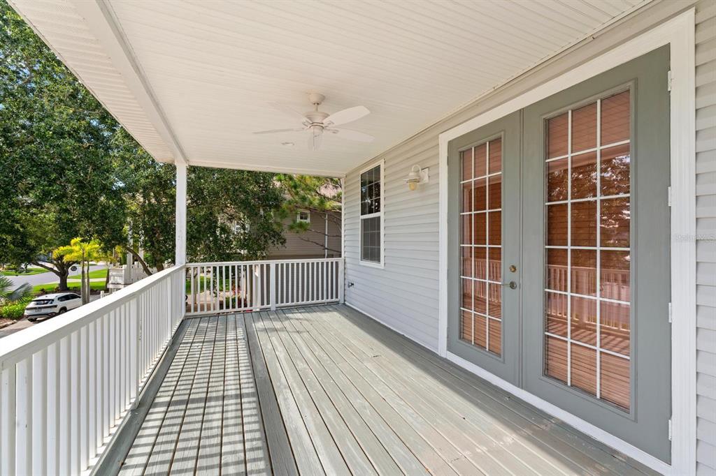 A covered wooden balcony features a ceiling fan, white railings, and gray French doors — 921 POINT SEASIDE DRIVE, CRYSTAL BEACH, FL