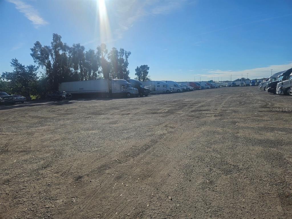 A large, unpaved dirt lot filled with parked semi-trucks and trailers under a sunny sky — 12355 US HWY 19 N, CLEARWATER, FL