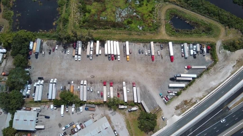 An aerial view shows a gravel lot filled with numerous semi-trucks and trailers near a highway — 12355 US HWY 19 N, CLEARWATER, FL