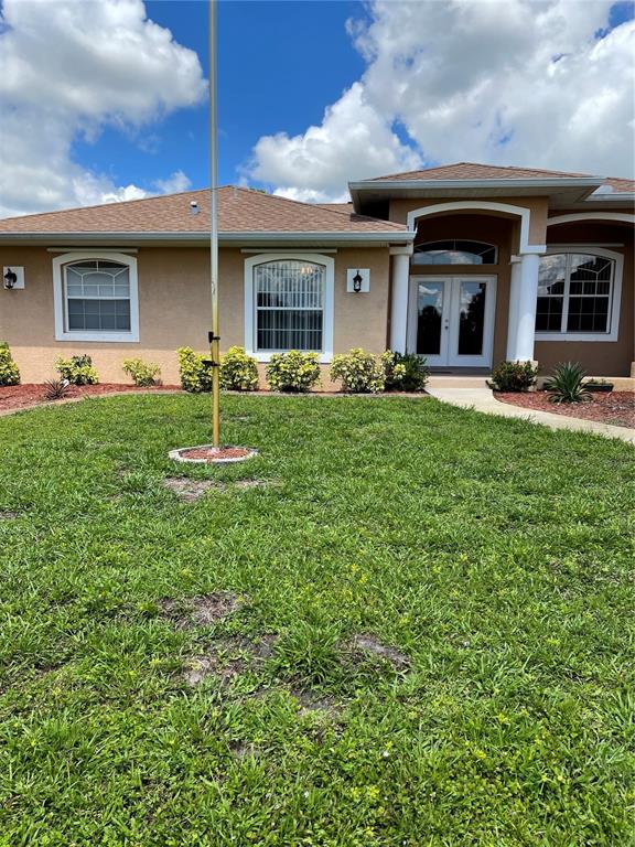 The exterior of a tan, single-story house features a front lawn and a flagpole — 9461 MIAMI CIRCLE, PORT CHARLOTTE, FL