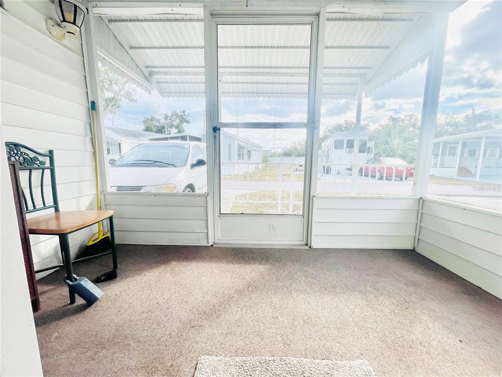 A screened-in porch features a carpeted floor, a metal chair, and a white screen door — 3275 26TH AVENUE E UNIT 107, BRADENTON, FL