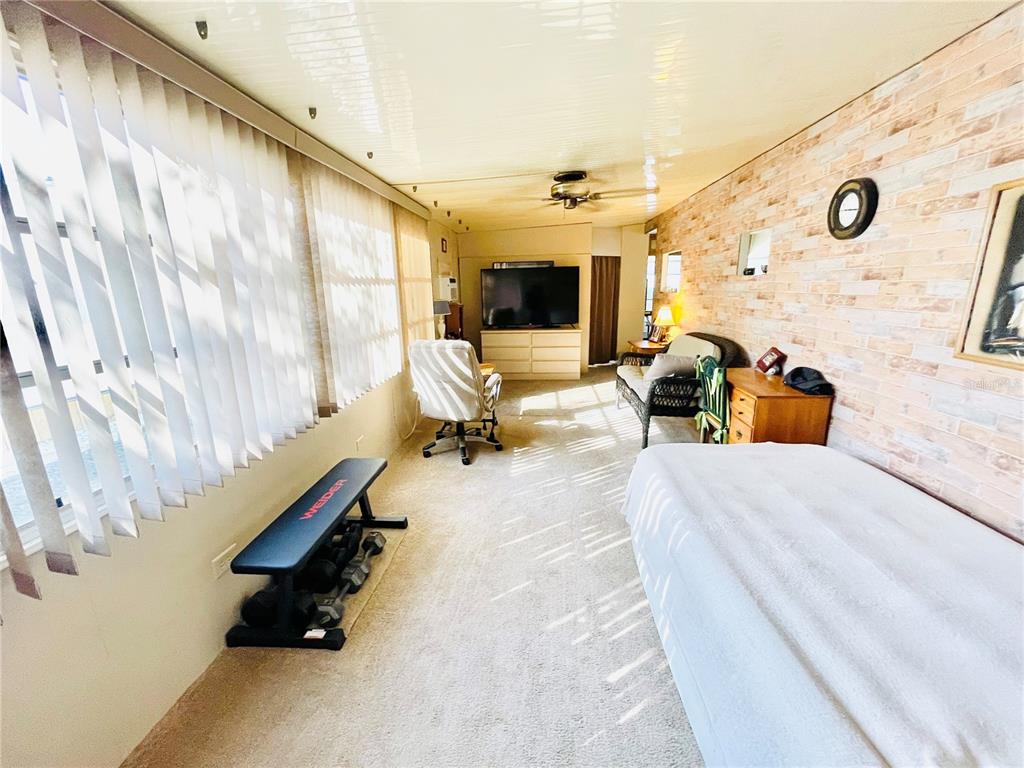 A sunroom features a brick accent wall, carpeted flooring, a television, and exercise equipment — 3275 26TH AVENUE E UNIT 107, BRADENTON, FL