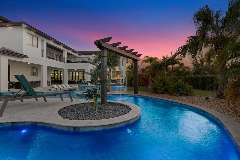 A backyard swimming pool features a waterfall structure and a lounge area at sunset — 1148 GRAND TRAVERSE PARKWAY, REUNION, FL