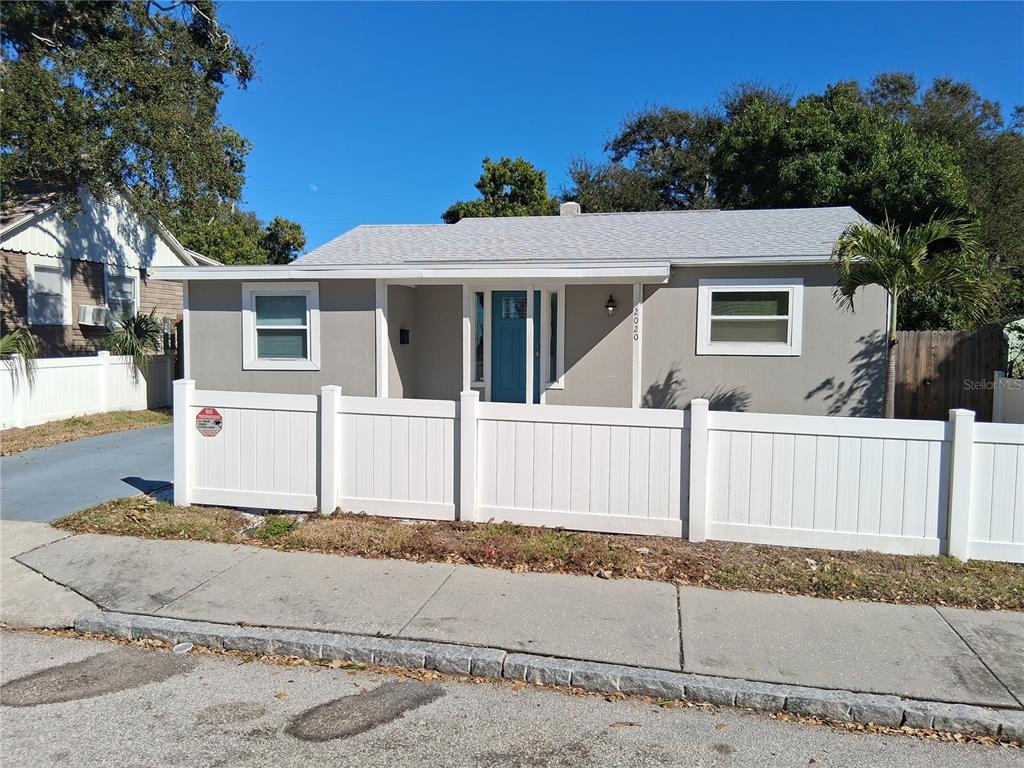 A single-story house with gray siding and a white fence stands behind a sidewalk — 2020 13TH STREET S, ST PETERSBURG, FL