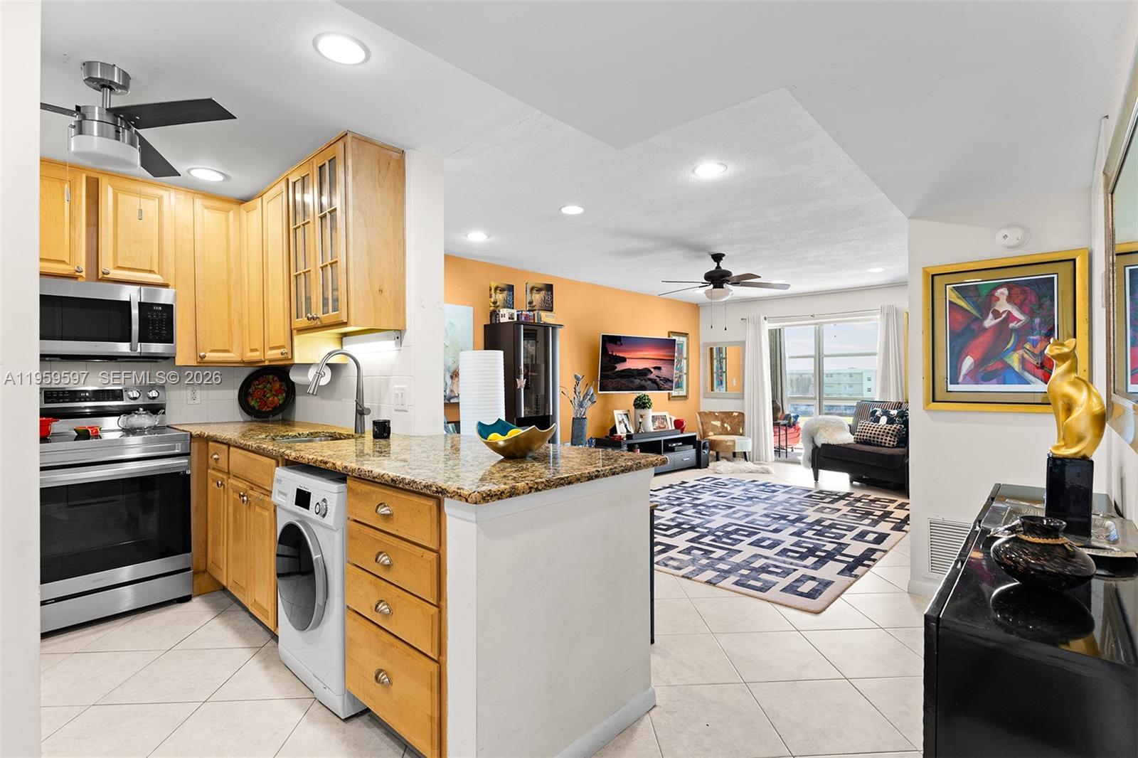 A kitchen with light wood cabinets and granite countertops opens into a living room area — 130 NE 26th Ave # 4040, Boynton Beach FL 33435, BOYNTON BEACH, FL