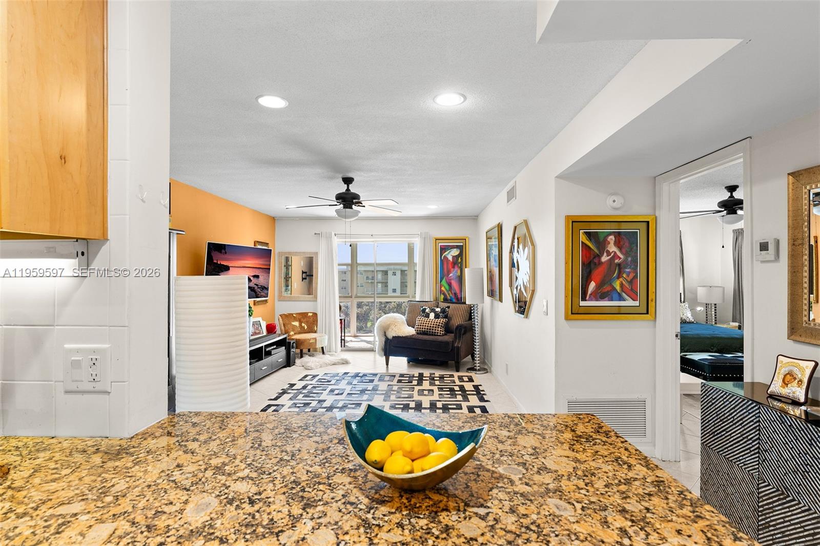 A granite kitchen counter with a bowl of lemons overlooks a living room with balcony access — 130 NE 26th Ave # 4040, Boynton Beach FL 33435, BOYNTON BEACH, FL