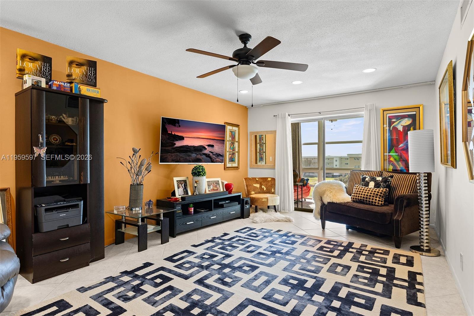A living room features an orange accent wall, a ceiling fan, and a patterned area rug — 130 NE 26th Ave # 4040, Boynton Beach FL 33435, BOYNTON BEACH, FL