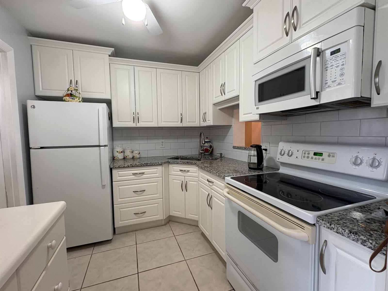 A white kitchen features granite countertops, white cabinets, a refrigerator, and a glass-top stove — 108 NE 20th Avenue NE # 206, Boynton Beach FL 33435, BOYNTON BEACH, FL