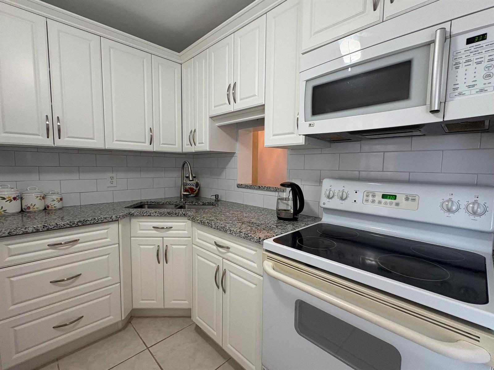 A kitchen features white cabinets, granite countertops, a white stove, and a subway tile backsplash — 108 NE 20th Avenue NE # 206, Boynton Beach FL 33435, BOYNTON BEACH, FL