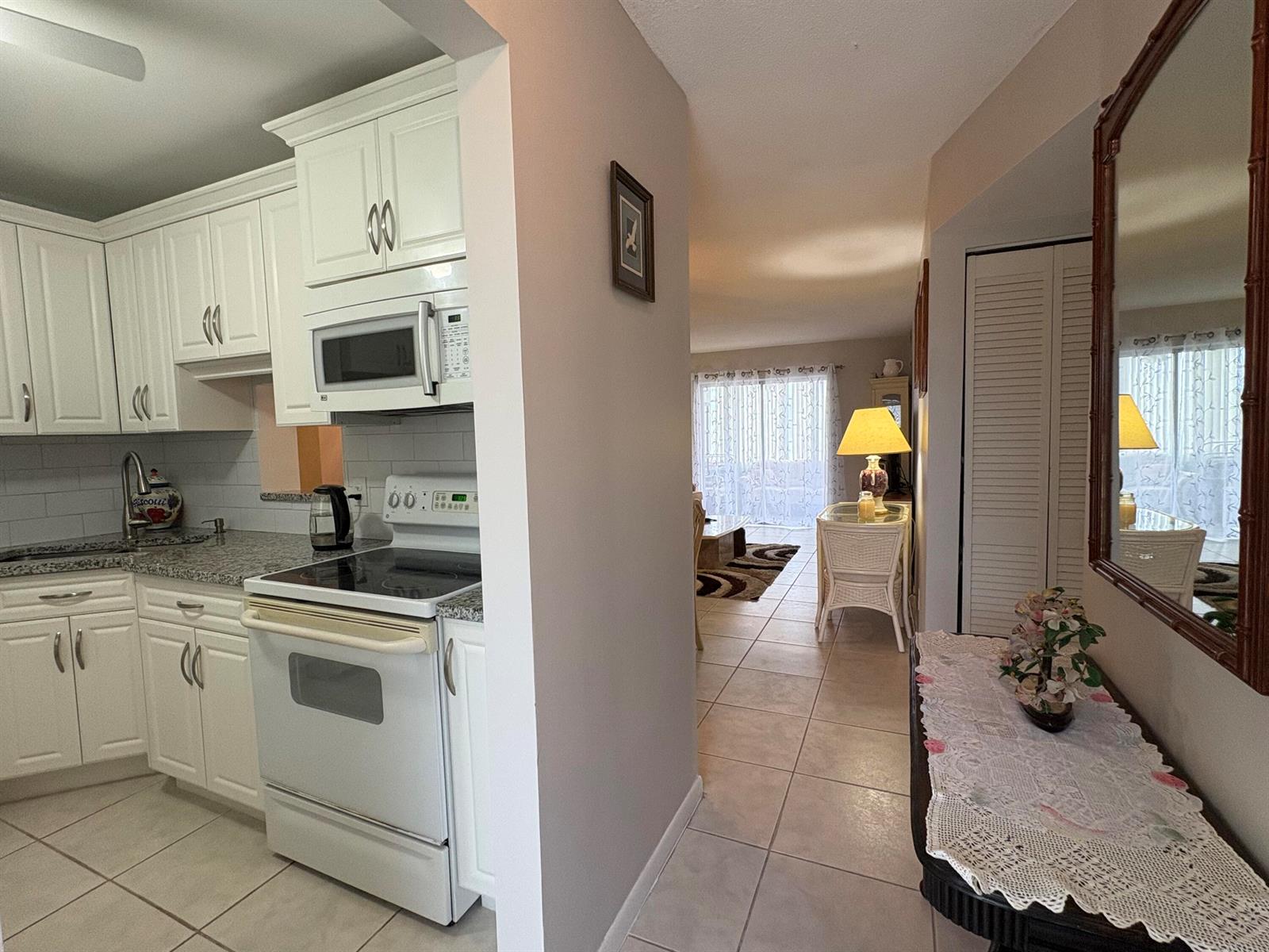 A white kitchen with granite countertops opens into a living area with tiled floors — 108 NE 20th Avenue NE # 206, Boynton Beach FL 33435, BOYNTON BEACH, FL