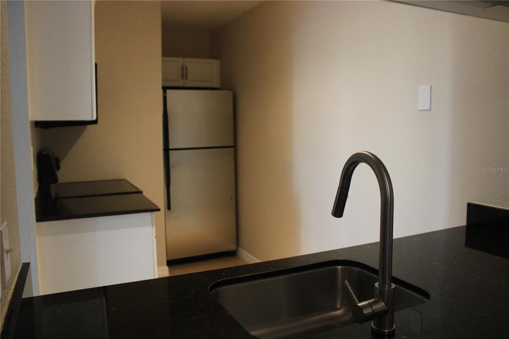 A kitchen features a stainless steel sink, dark countertops, and a stainless steel refrigerator — 3300 HAVILAND COURT UNIT 104, PALM HARBOR, FL