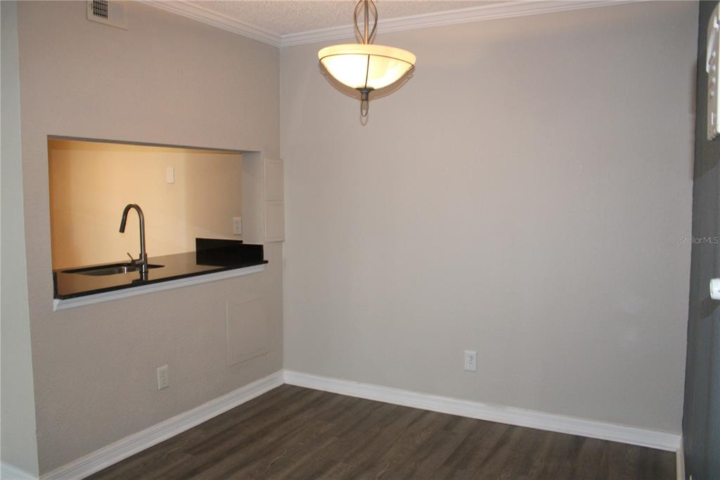 A dining area with wood-look flooring, a pendant light, and a kitchen pass-through window — 3300 HAVILAND COURT UNIT 104, PALM HARBOR, FL