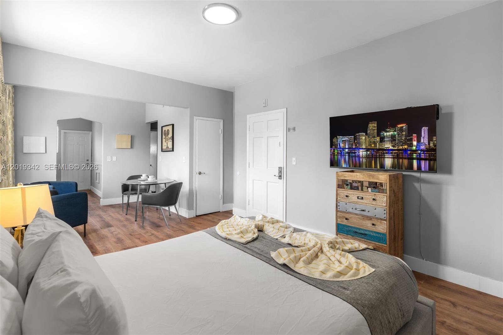A bedroom features a bed, a wall-mounted television, a wooden dresser, and a dining area — 8100 Harding Ave # 514, Miami Beach FL 33141, MIAMI BEACH, FL