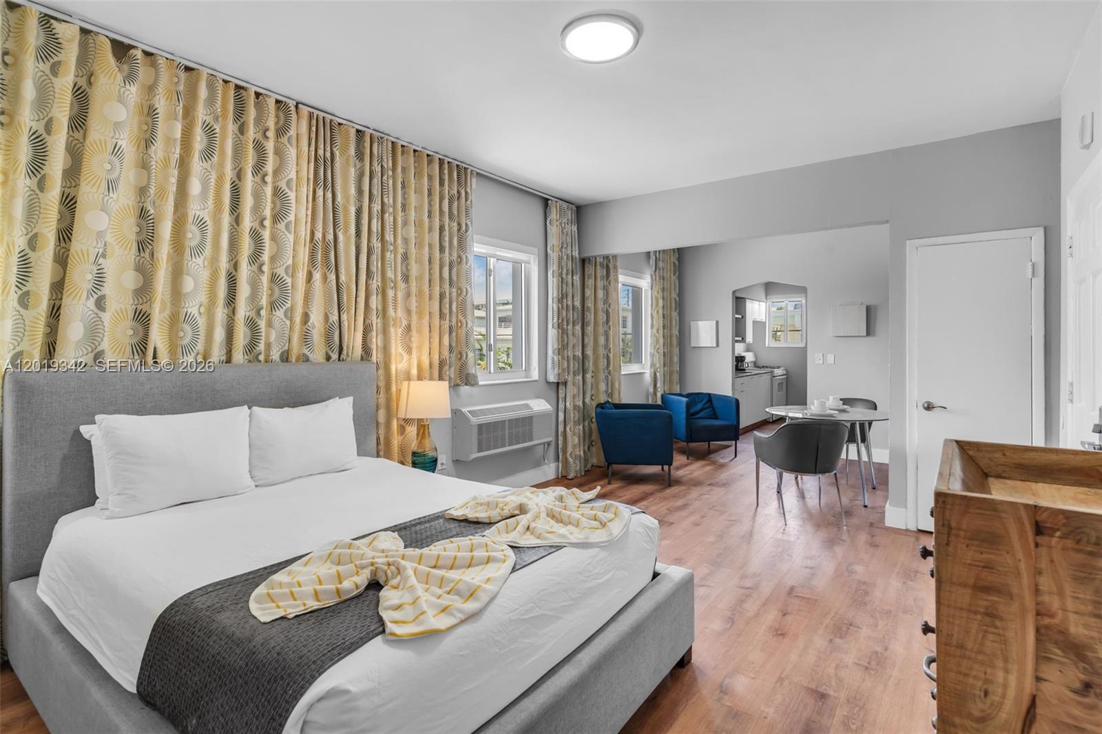 A bedroom features a gray bed, patterned curtains, blue armchairs, and a small dining area — 8100 Harding Ave # 514, Miami Beach FL 33141, MIAMI BEACH, FL