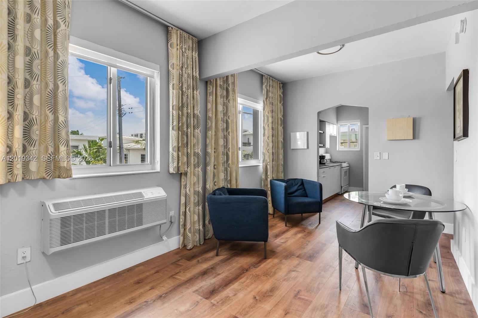 A living and dining area features wood-look flooring, two blue armchairs, and a glass table — 8100 Harding Ave # 514, Miami Beach FL 33141, MIAMI BEACH, FL
