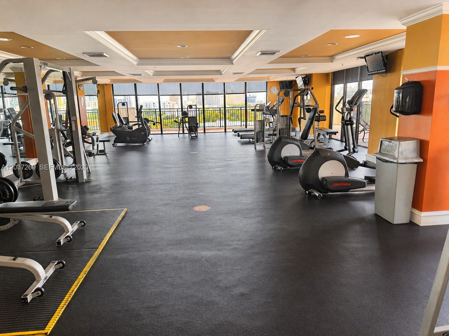 A gym features various exercise machines, rubber flooring, and large windows overlooking a city view — 888 S Douglas Rd # 1602, Coral Gables FL 33134, CORAL GABLES, FL