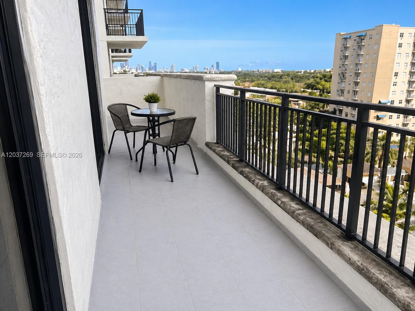 A balcony features gray tile flooring, a small bistro set, and a black metal railing — 888 S Douglas Rd # 1602, Coral Gables FL 33134, CORAL GABLES, FL