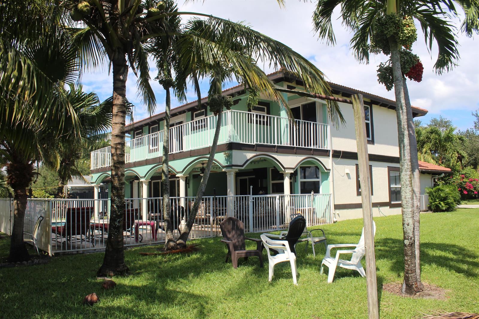 A two-story house with a balcony, arched patio, and pool area surrounded by palm trees — 13847 Geranium Place, Wellington FL 33414, WELLINGTON, FL