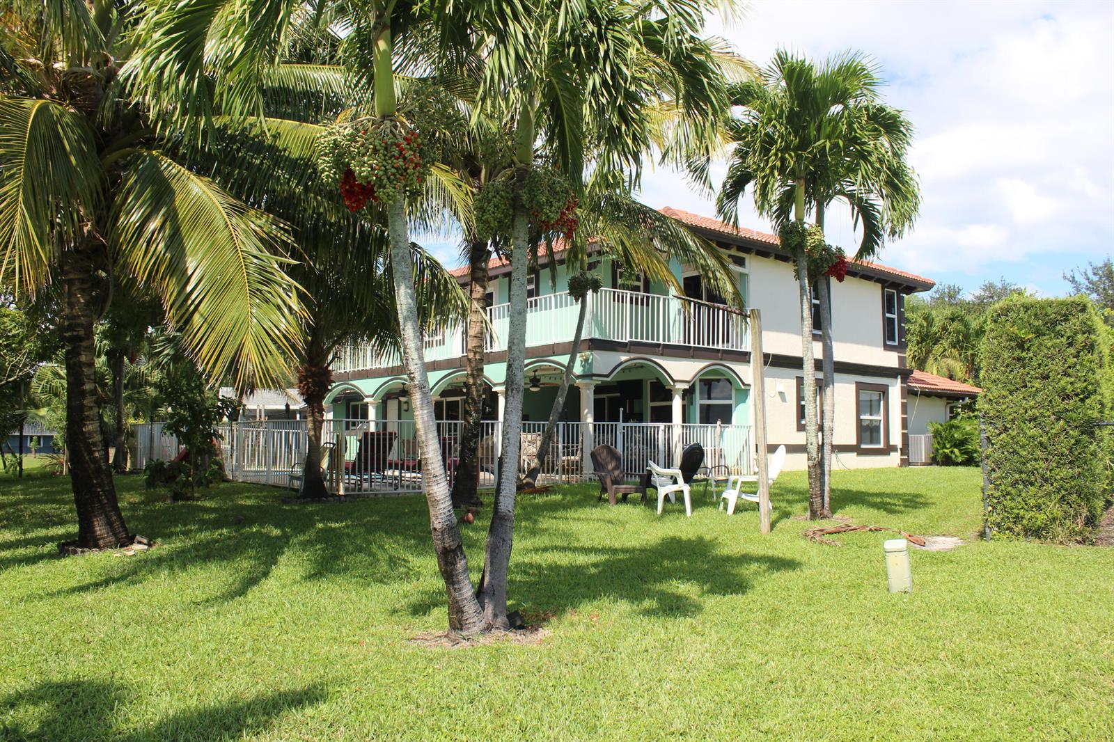 A two-story house with a balcony and patio overlooks a grassy backyard with palm trees — 13847 Geranium Place, Wellington FL 33414, WELLINGTON, FL