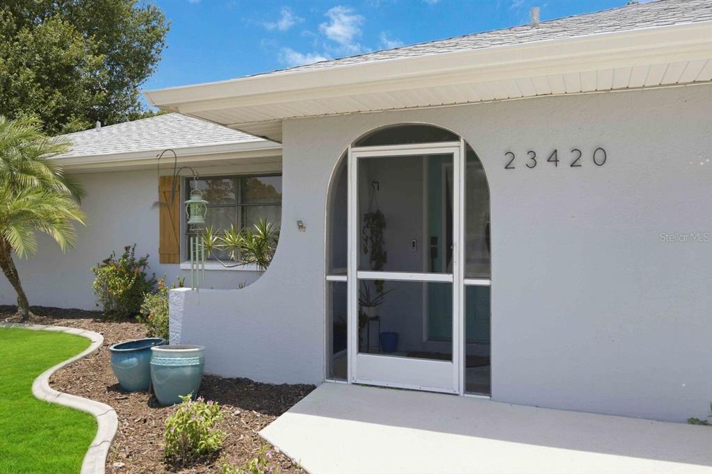 The exterior of a light-colored house features a white arched screen door and address numbers — 23420 STEEPLE AVENUE, PORT CHARLOTTE, FL