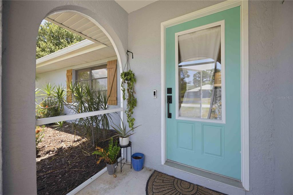 A light blue front door sits under a covered entryway with a potted plant nearby — 23420 STEEPLE AVENUE, PORT CHARLOTTE, FL