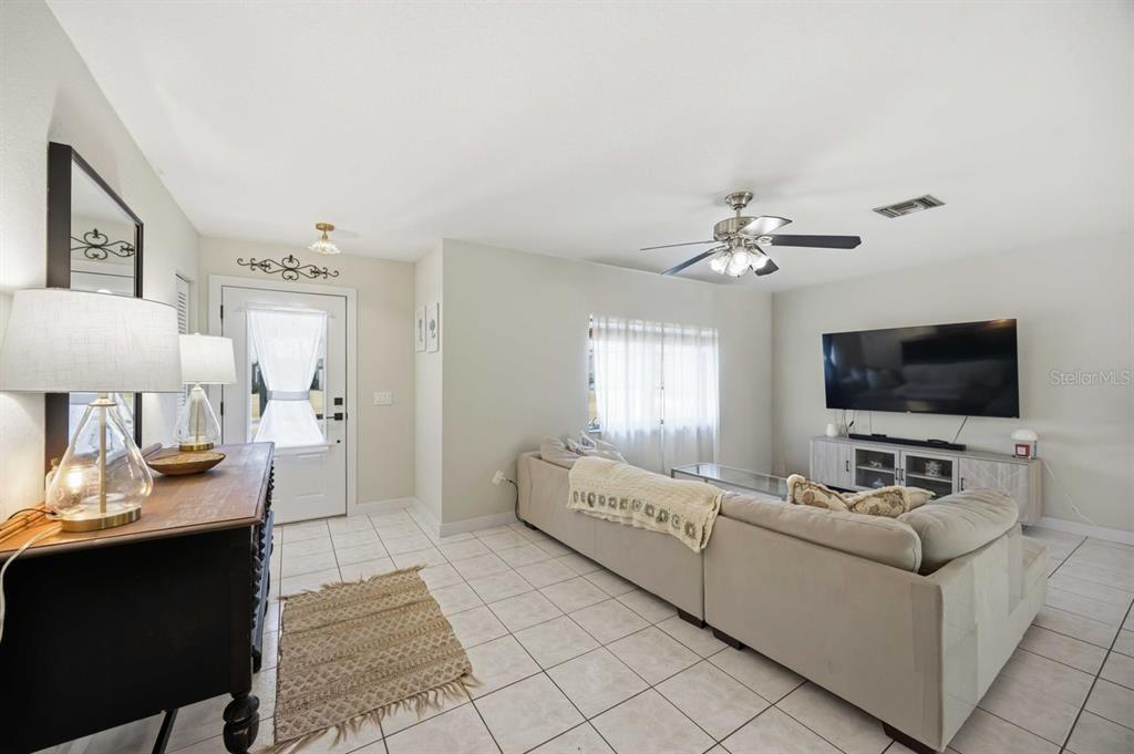 A living room features tile flooring, a beige sectional sofa, and a wall-mounted television — 23420 STEEPLE AVENUE, PORT CHARLOTTE, FL