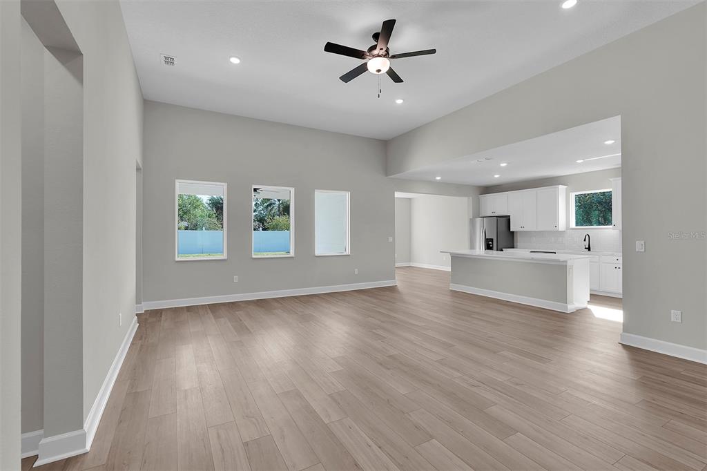 An open-concept living room with light wood flooring, a ceiling fan, and a white kitchen — 3 FIELDING LANE, PALM COAST, FL