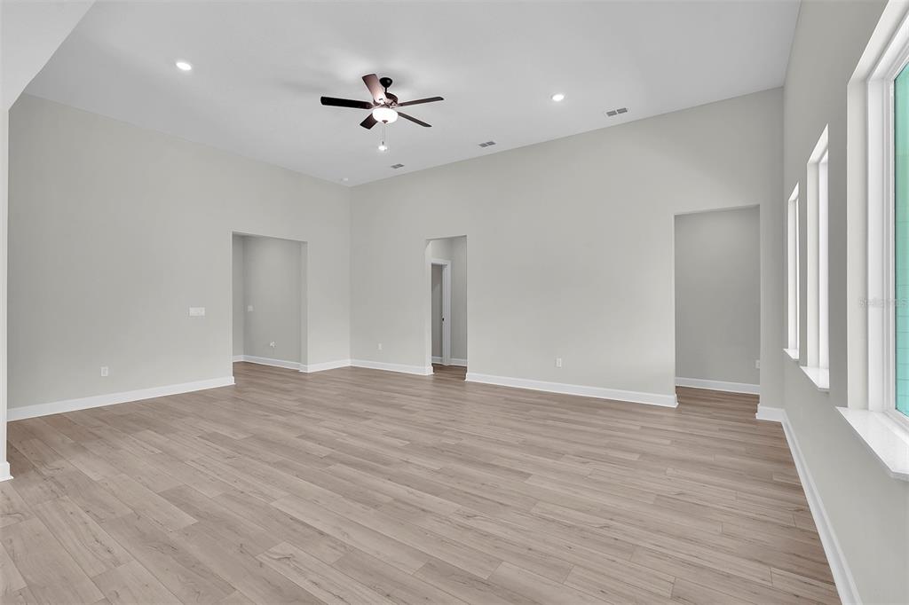 An empty room with light wood-look flooring, white walls, a ceiling fan, and three windows — 3 FIELDING LANE, PALM COAST, FL