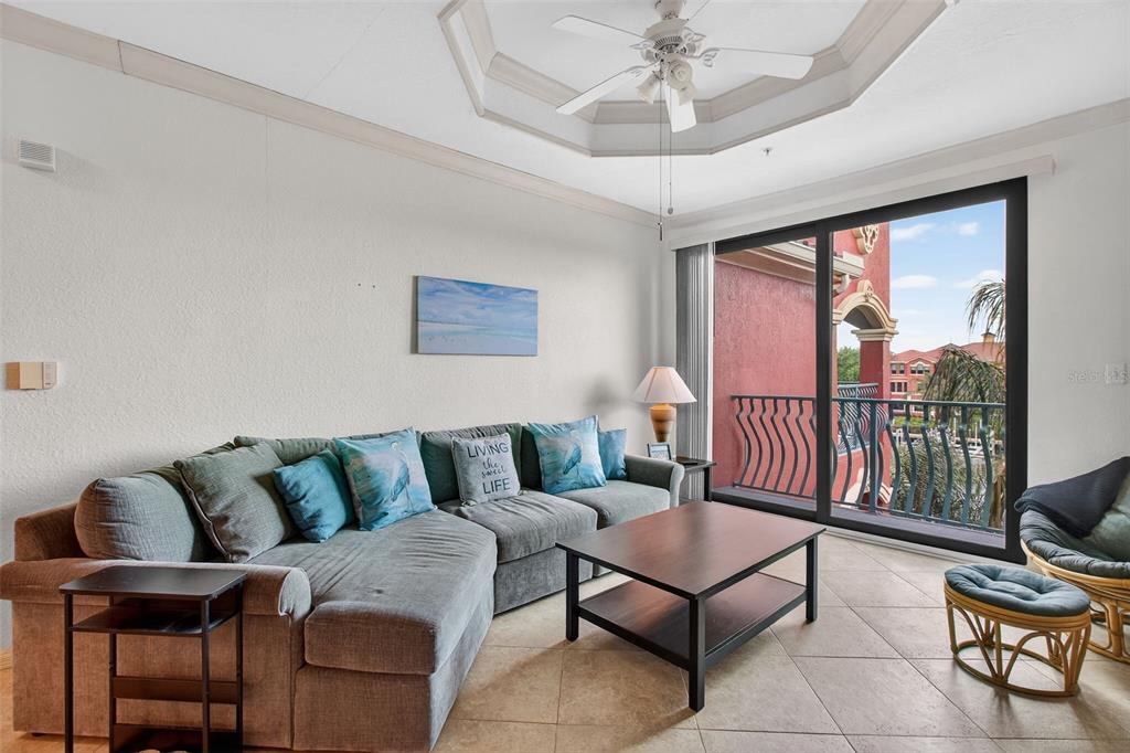 A living room features a gray sectional sofa, a coffee table, and a balcony view — 2730 VIA TIVOLI UNIT 335A, CLEARWATER, FL