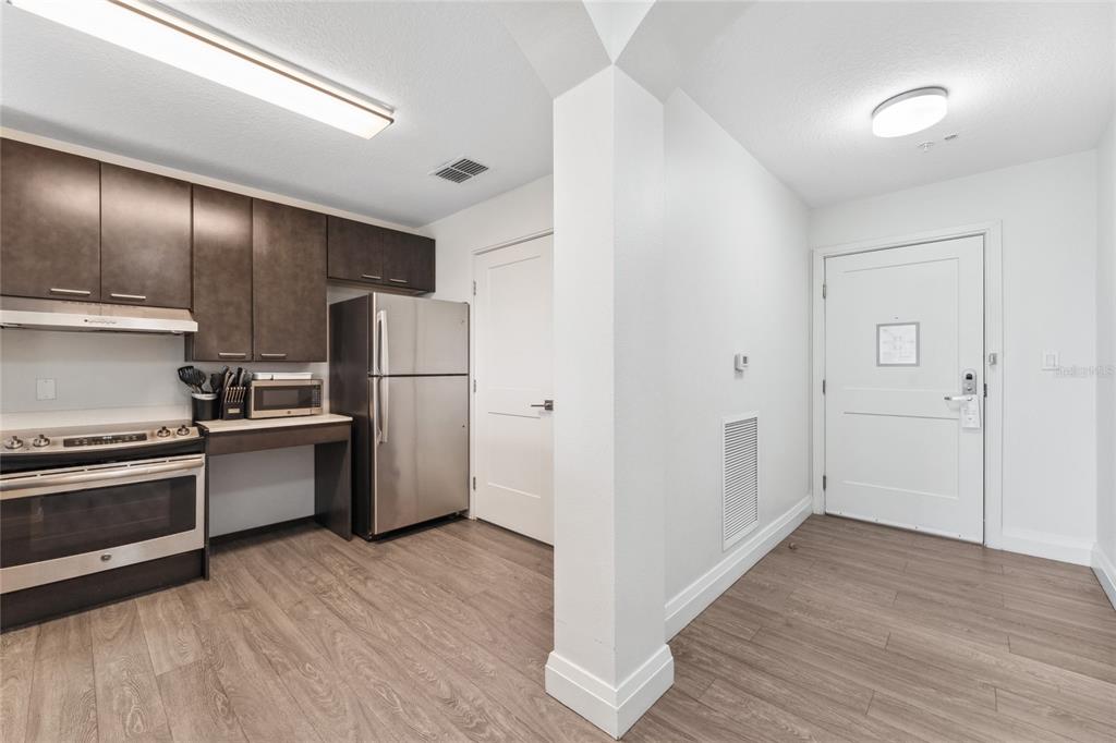 A kitchen with stainless steel appliances and dark cabinets sits next to an entryway door — 14501 GROVE RESORT AVENUE UNIT 3642, WINTER GARDEN, FL
