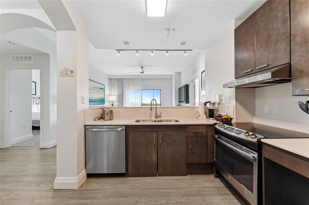 A kitchen with dark wood cabinets, stainless steel appliances, and a view into the living area — 14501 GROVE RESORT AVENUE UNIT 3642, WINTER GARDEN, FL