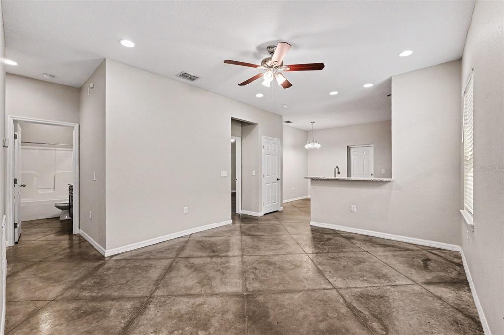 An open-concept living area features stained concrete floors, a ceiling fan, and a kitchen pass-through — 2865 WHISPERING TRAILS DRIVE, WINTER HAVEN, FL