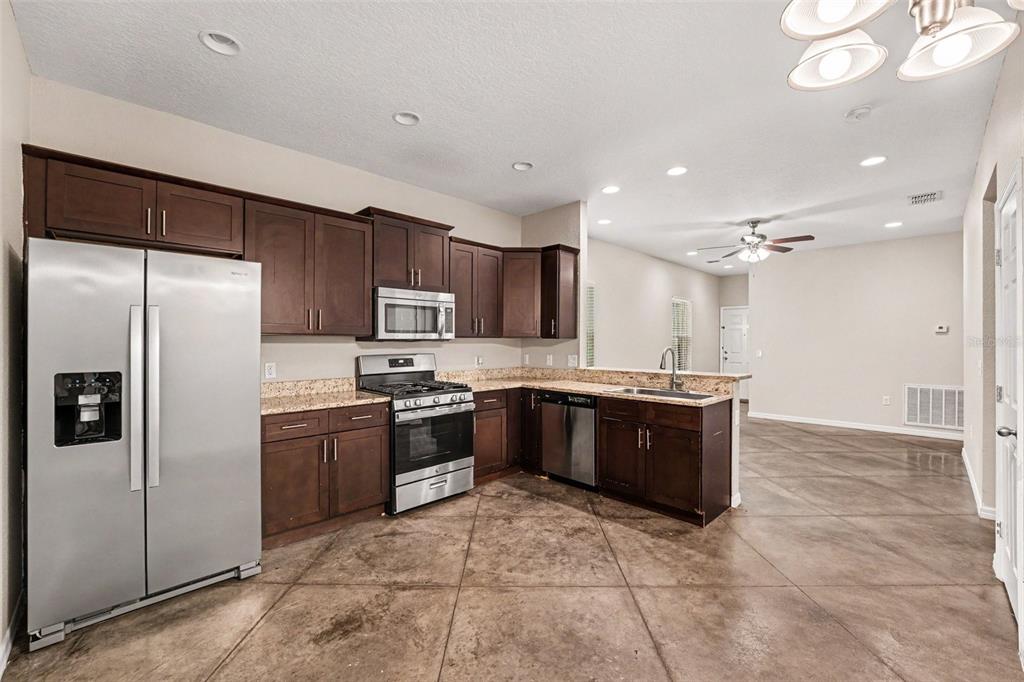 A kitchen with dark wood cabinets, stainless steel appliances, and brown tile flooring — 2865 WHISPERING TRAILS DRIVE, WINTER HAVEN, FL
