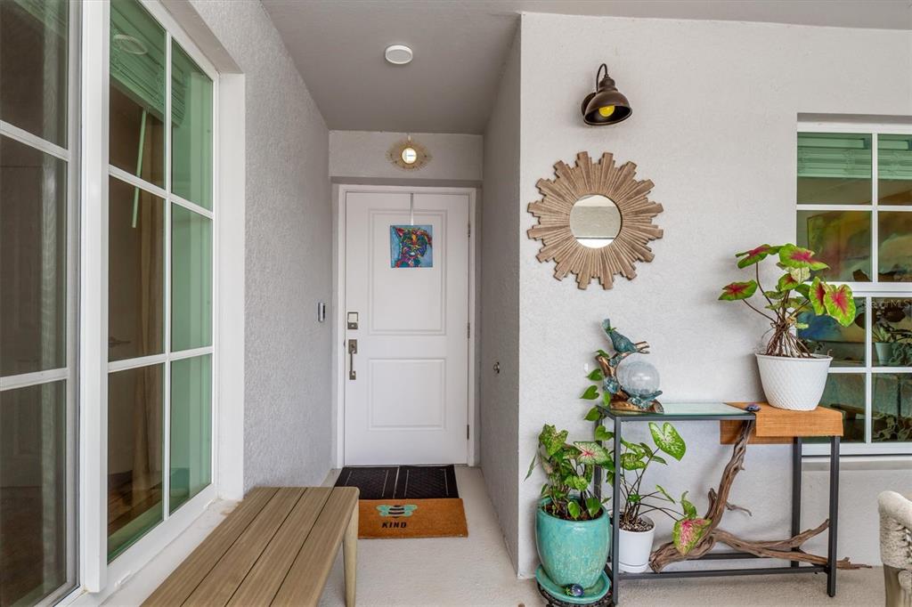 A covered entryway features a white front door, a wooden bench, and a decorative console table — 14221 HERITAGE LANDING BOULEVARD UNIT 2026, PUNTA GORDA, FL