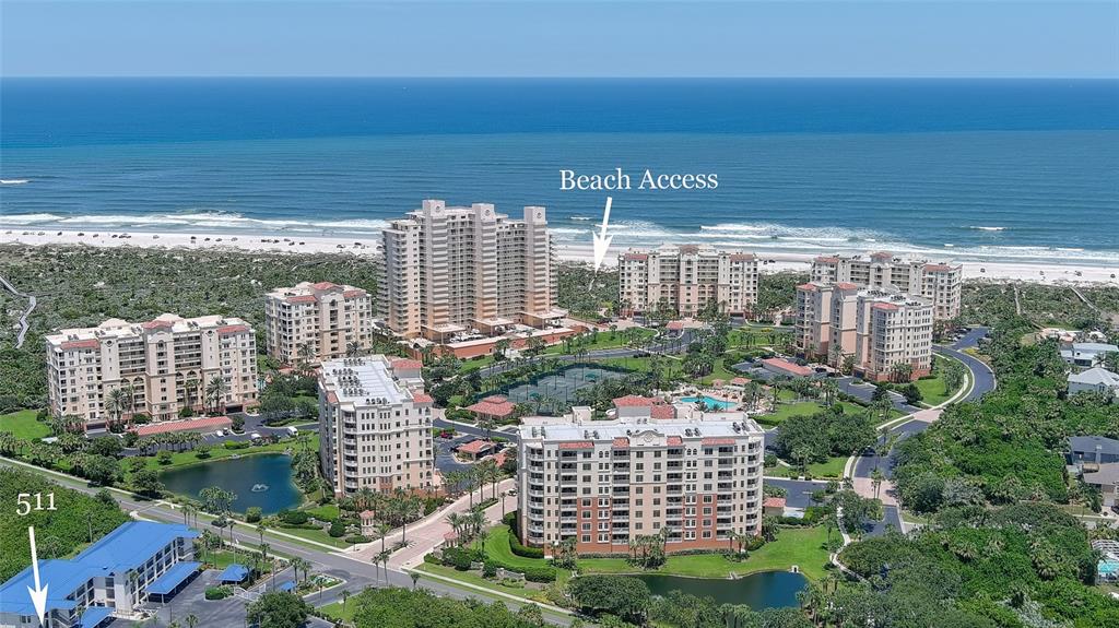 An aerial view shows several multi-story residential buildings surrounded by greenery and a nearby beach — 2700 N PENINSULA AVENUE UNIT 511, NEW SMYRNA BEACH, FL