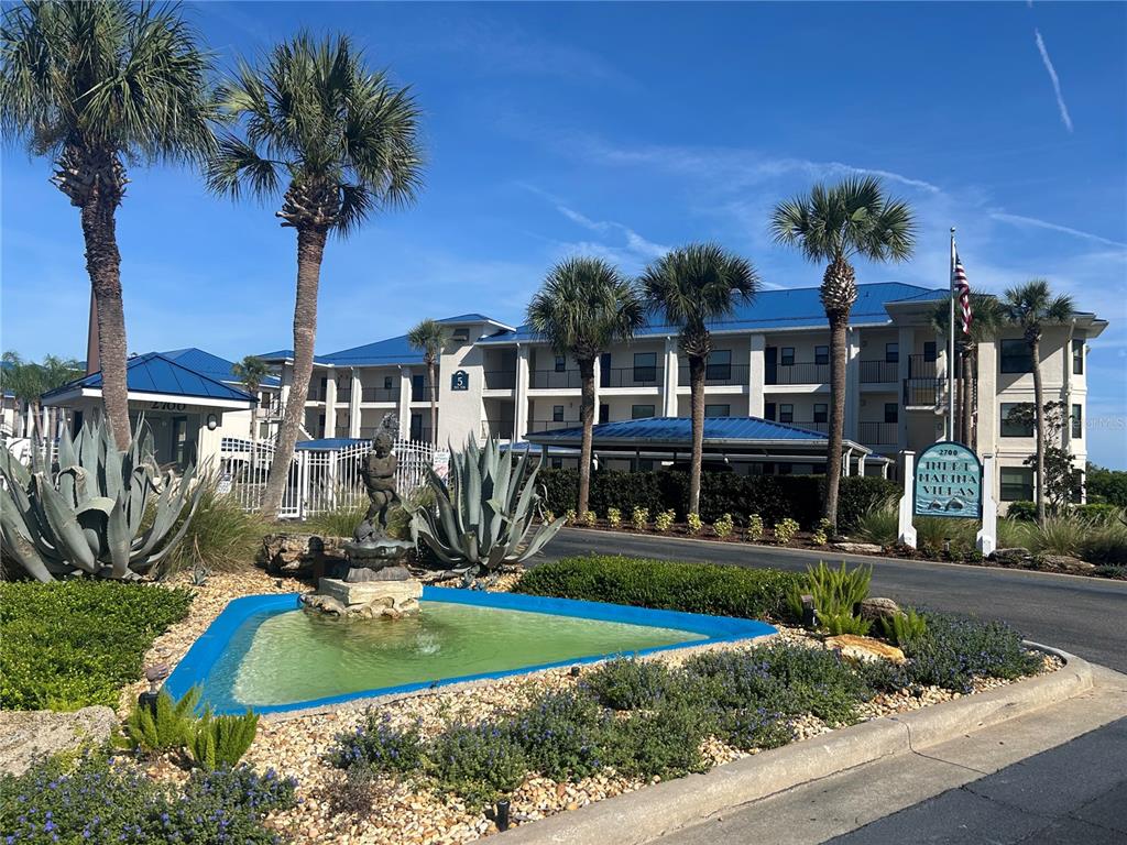An exterior view of a multi-story apartment complex with palm trees and a decorative fountain — 2700 N PENINSULA AVENUE UNIT 511, NEW SMYRNA BEACH, FL