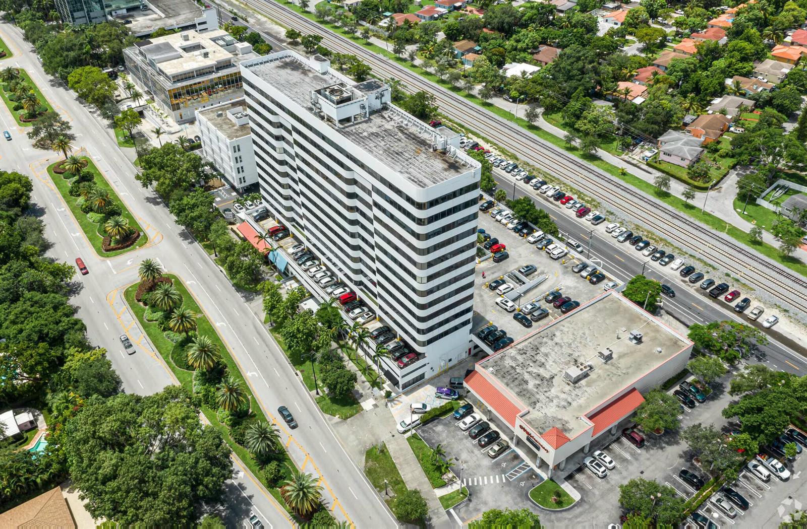 An aerial view shows a tall white office building with adjacent parking and a retail store — 4770 Biscayne Boulevard # 620, Miami FL 33137, MIAMI, FL