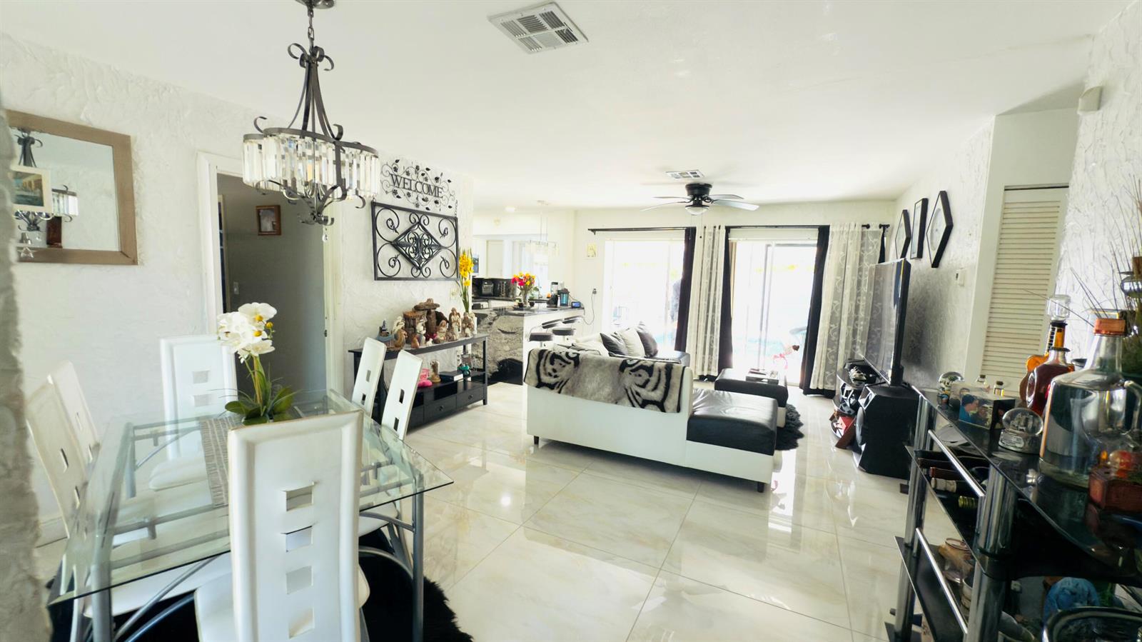 An open-concept living and dining area features white tile flooring, a glass table, and furniture — 230 NE 25th Street, Pompano Beach FL 33064, POMPANO BEACH, FL