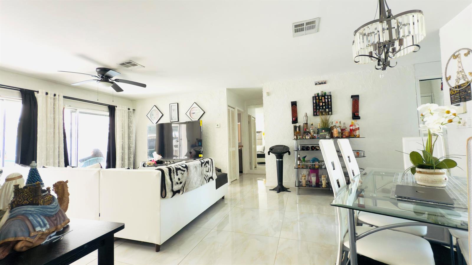 A bright living and dining area features white tile floors, a sectional sofa, and chandelier — 230 NE 25th Street, Pompano Beach FL 33064, POMPANO BEACH, FL