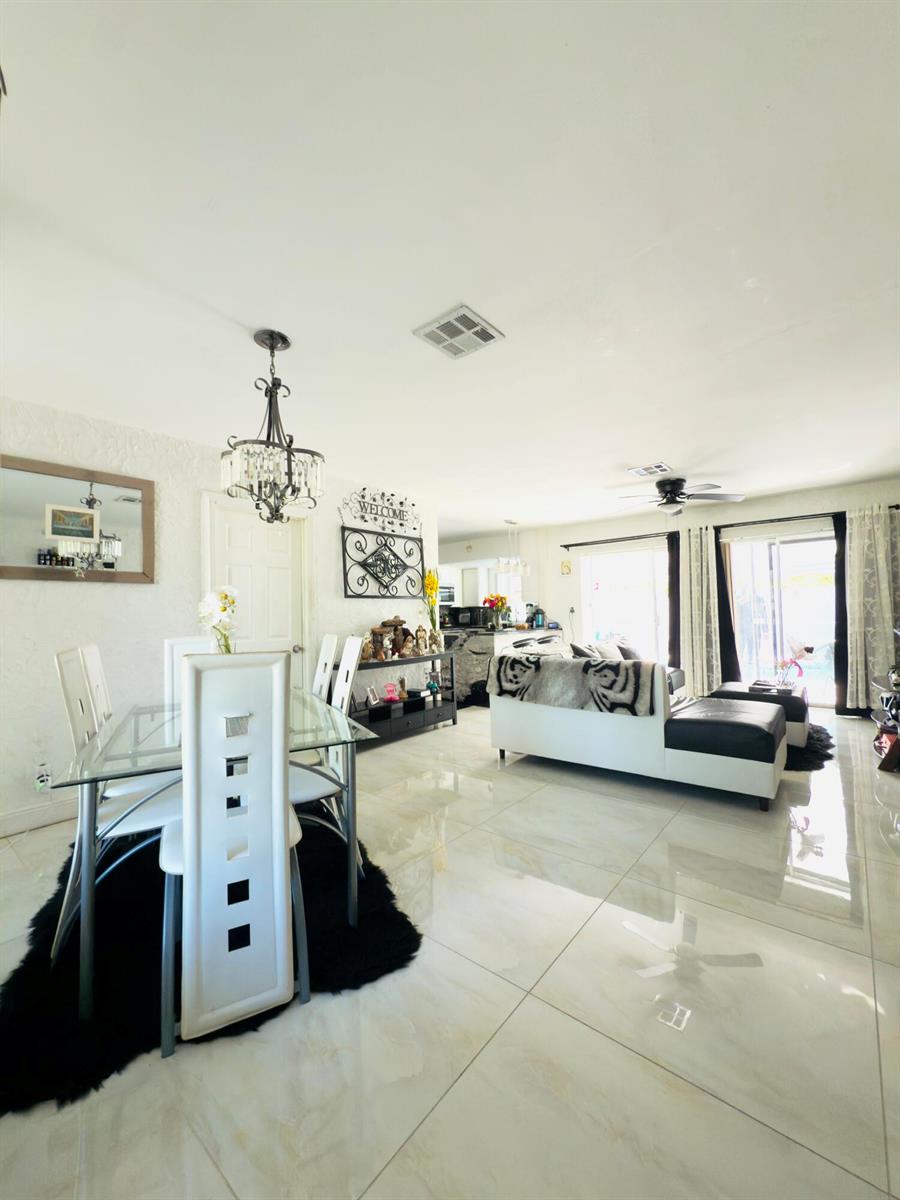 A dining area with a glass table and white chairs opens into a living room — 230 NE 25th Street, Pompano Beach FL 33064, POMPANO BEACH, FL