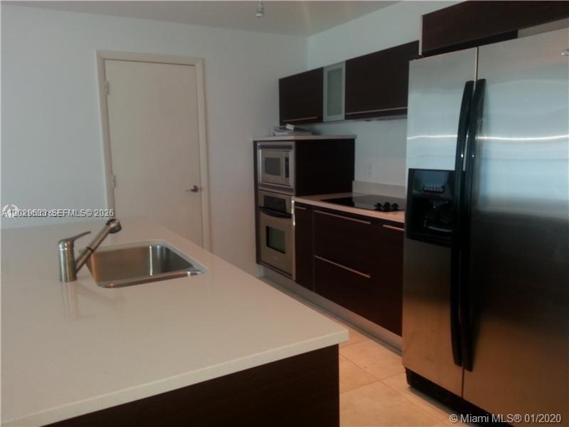 A modern kitchen features dark wood cabinetry, stainless steel appliances, and a white island countertop — 1900 N Bayshore Dr # 3517, Miami FL 33132, MIAMI, FL