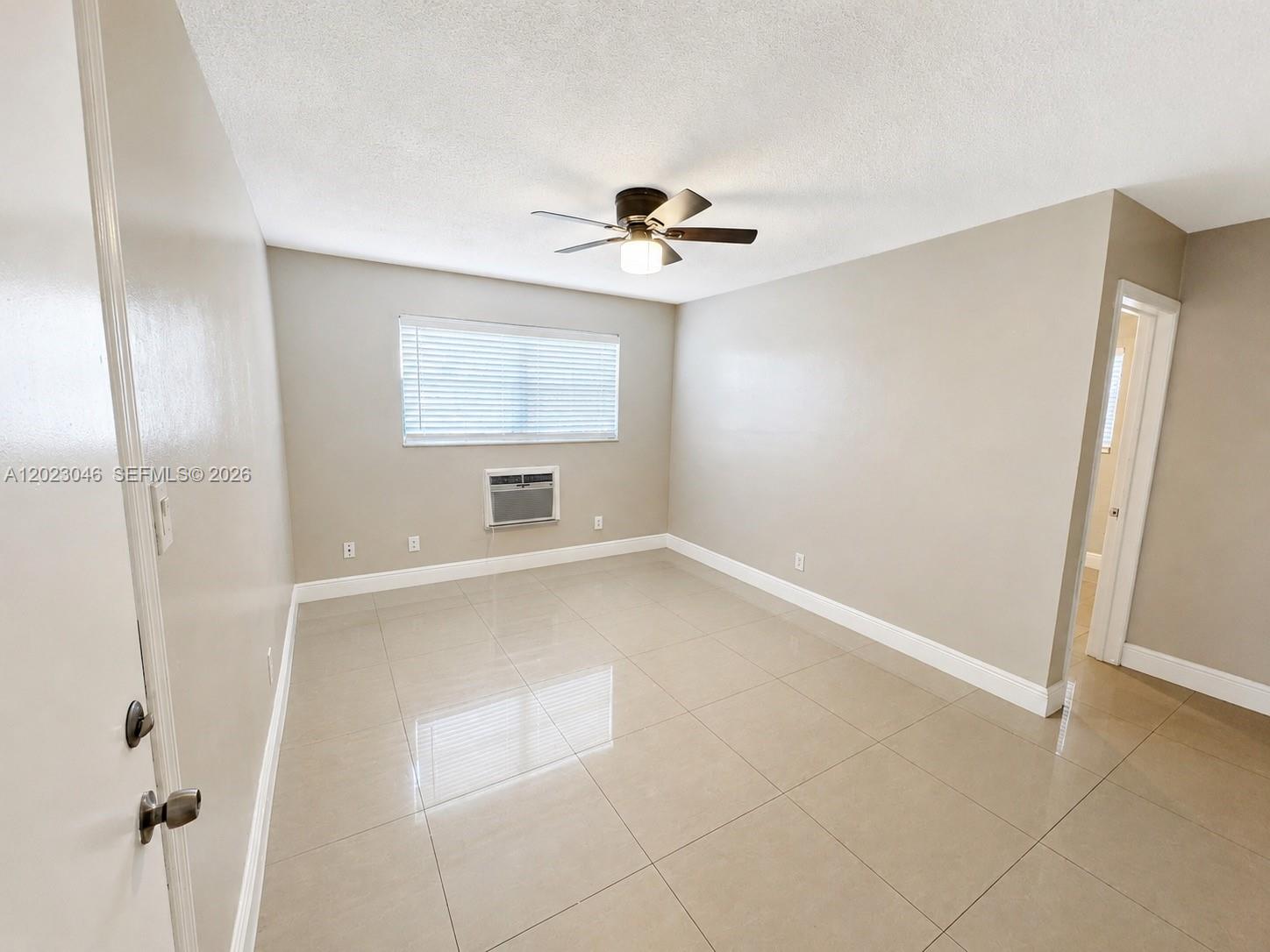 An empty room features beige tile flooring, light-colored walls, a ceiling fan, and a window unit — 811 NW 6th Ave # 4, Pompano Beach FL 33060, POMPANO BEACH, FL