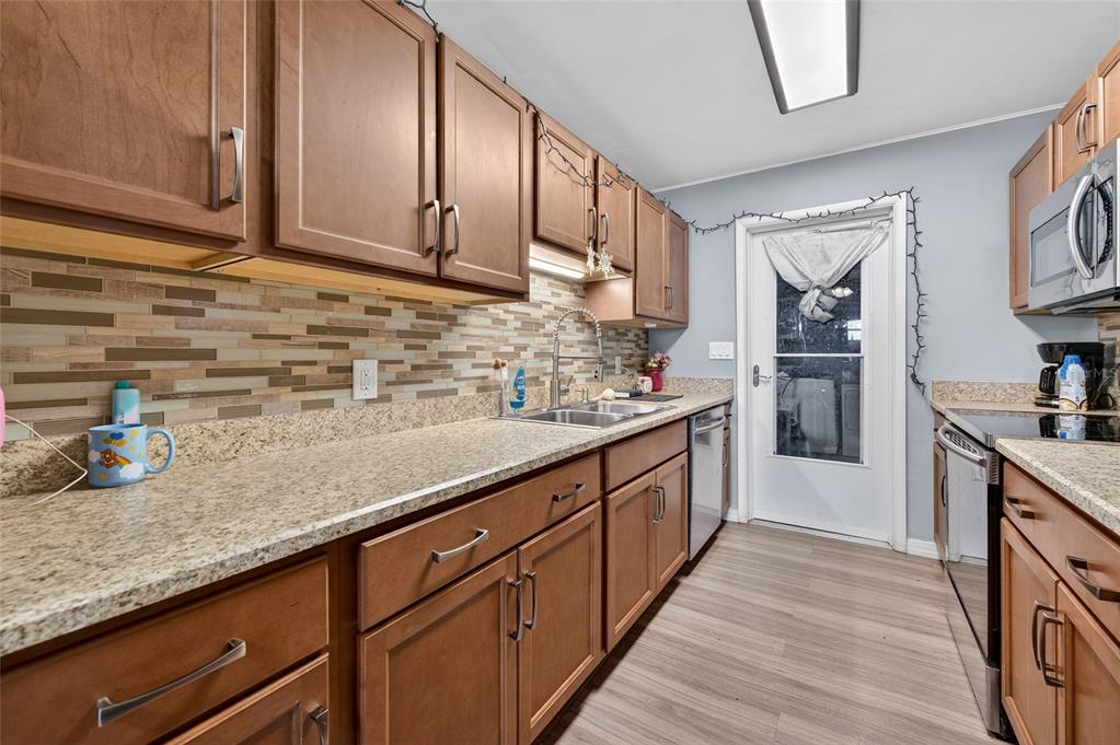 A kitchen features wood cabinets, granite countertops, a tiled backsplash, and stainless steel appliances — 729 N FLAMINGO DRIVE, HOLLY HILL, FL