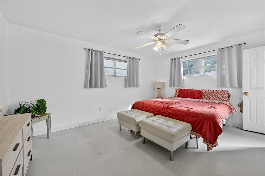 A bedroom features white walls, a red bedspread, two white ottomans, and a ceiling fan — 729 N FLAMINGO DRIVE, HOLLY HILL, FL