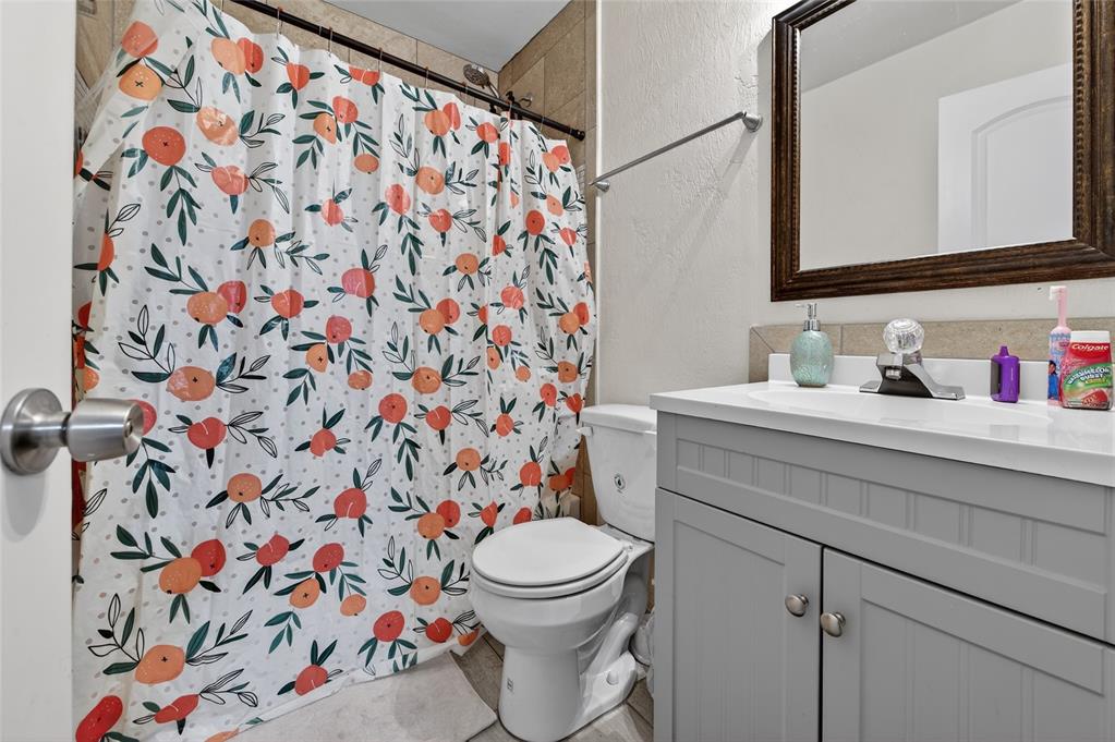A bathroom features a gray vanity, a white toilet, and a peach-patterned shower curtain — 729 N FLAMINGO DRIVE, HOLLY HILL, FL